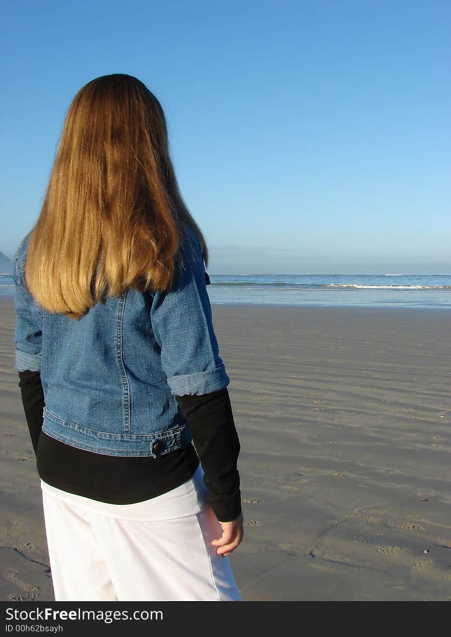 Young girl standing on the beach looking into the distance. Young girl standing on the beach looking into the distance