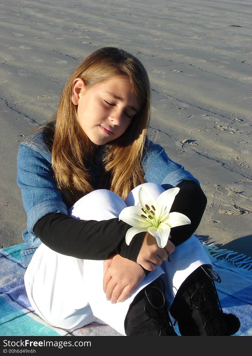 Young girl sitting on the beach with a flower in her hand, thinking of something. Young girl sitting on the beach with a flower in her hand, thinking of something