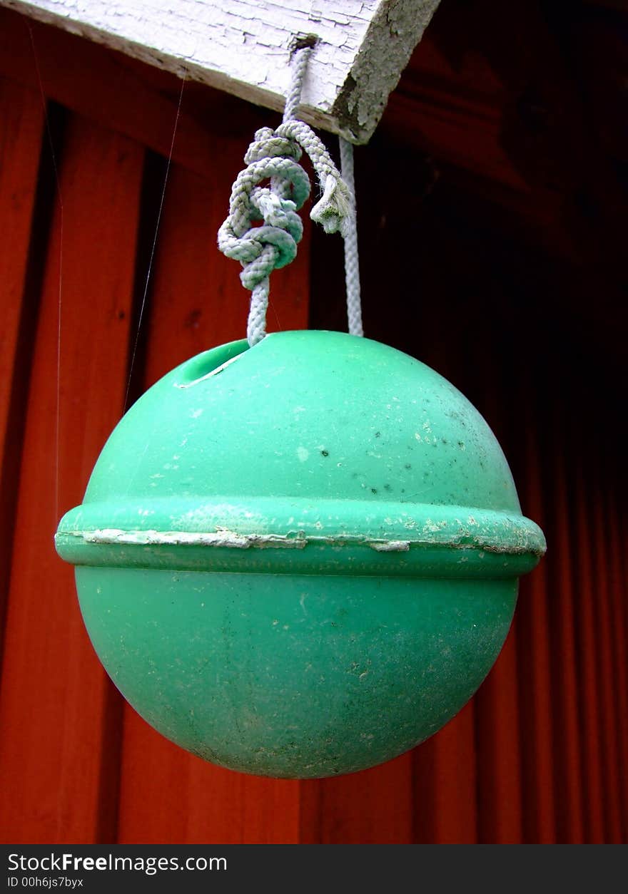 A green boatbuoy hanging from the roof of a red woodenhouse, Sweden.