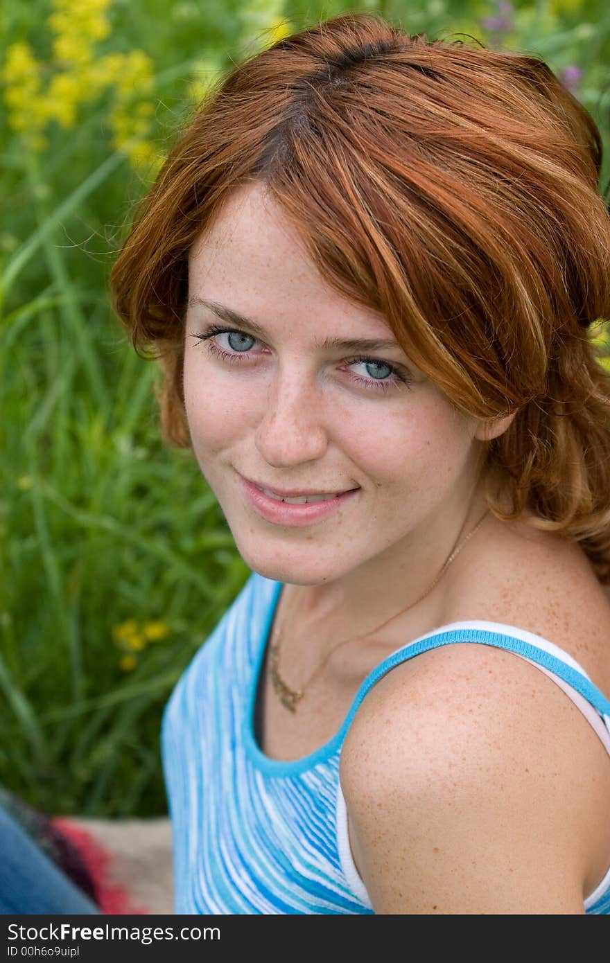 Outdoor shot of red-haired girl sitting on summer meadow and looking upward. Outdoor shot of red-haired girl sitting on summer meadow and looking upward