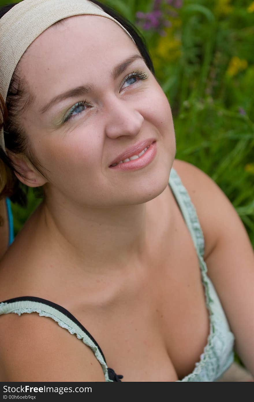 Outdoor shot of black-haired girl sitting on summer meadow and looking upward. Outdoor shot of black-haired girl sitting on summer meadow and looking upward