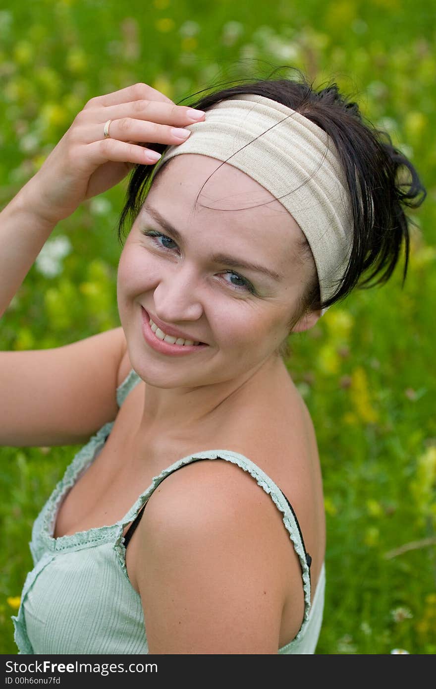 Outdoor shot of black-haired girl sitting on summer meadow and touching her head. Outdoor shot of black-haired girl sitting on summer meadow and touching her head