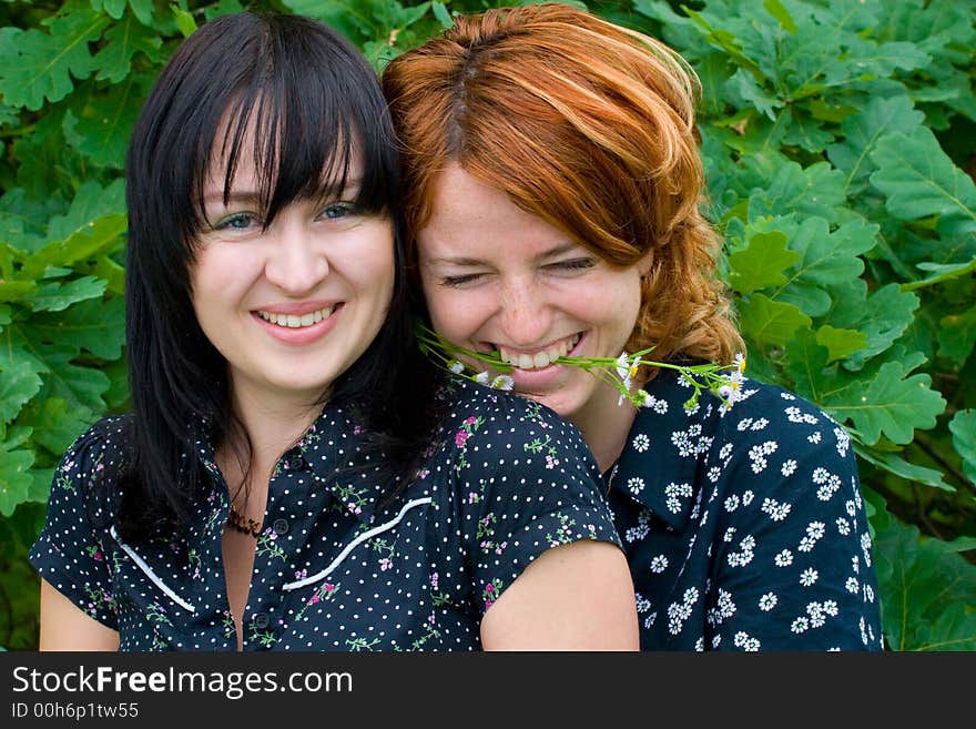 Two laughing girls on background of oak leaves. One girl keeps flower with teeth. Two laughing girls on background of oak leaves. One girl keeps flower with teeth