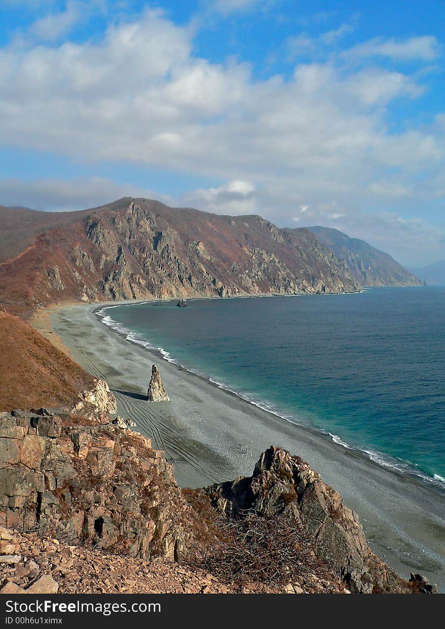 A cloudscape on sea: turquoise sea, grey beach, yellow-red capes and white clouds on azure sky. Autumn. Pastel. Vertical. Russian Far East, Primorye, Japanese sea, Tasovaya bay. A cloudscape on sea: turquoise sea, grey beach, yellow-red capes and white clouds on azure sky. Autumn. Pastel. Vertical. Russian Far East, Primorye, Japanese sea, Tasovaya bay.