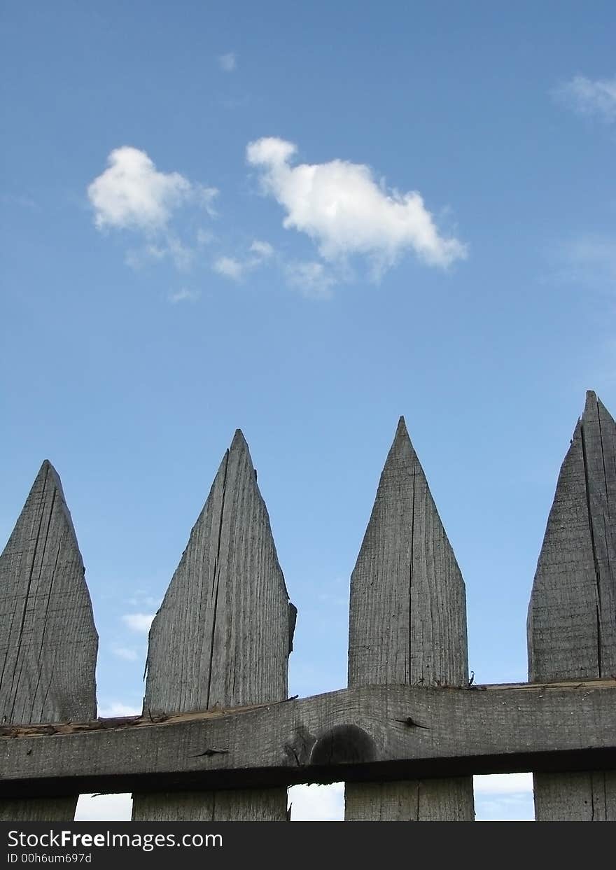 Fragment of the old wooden fence at the background of blue sky with clouds