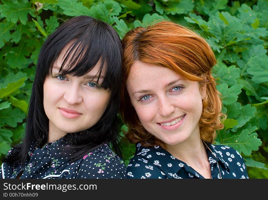 Two smiling girls on background of oak leaves. Two smiling girls on background of oak leaves