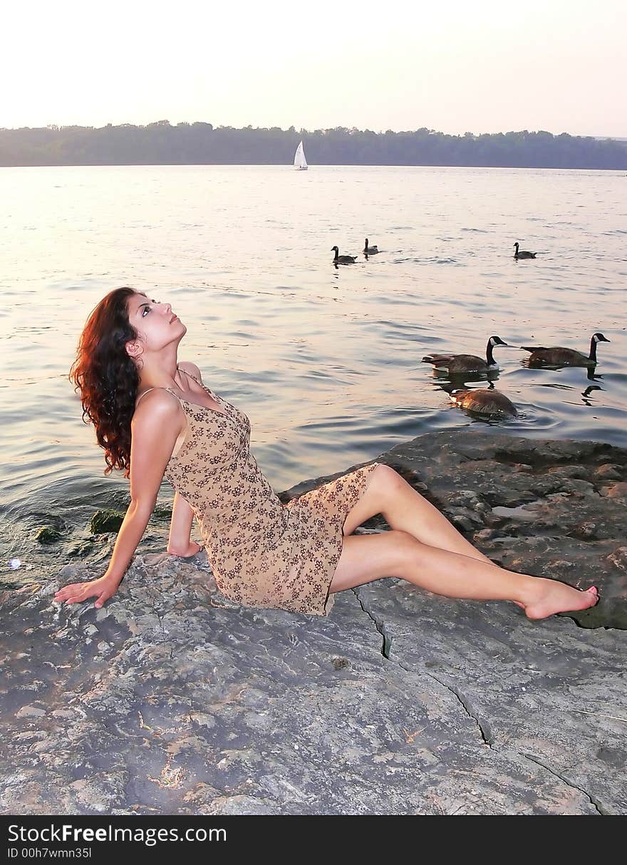 An lovely young lady sitting on a big rock on the lake relaxing by sunset. An lovely young lady sitting on a big rock on the lake relaxing by sunset.