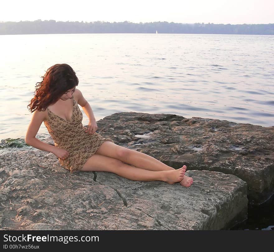 An lovely young lady sitting on a big rock on the lake and try to fix her
dress on a nice sunset. An lovely young lady sitting on a big rock on the lake and try to fix her
dress on a nice sunset.