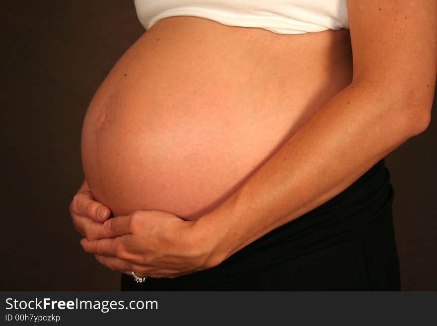 A woman tenderly holds her pregnant stomach. A woman tenderly holds her pregnant stomach.