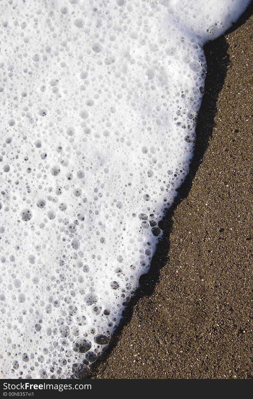 A small wave rolls up the sand like icing spreading on a sponge. A small wave rolls up the sand like icing spreading on a sponge