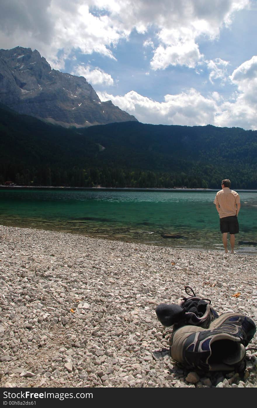 A young man cooling his feet off int he water of a beautiful lake in Bavaria, Germany...his sneakers and socks are laying int he foreground. A young man cooling his feet off int he water of a beautiful lake in Bavaria, Germany...his sneakers and socks are laying int he foreground.