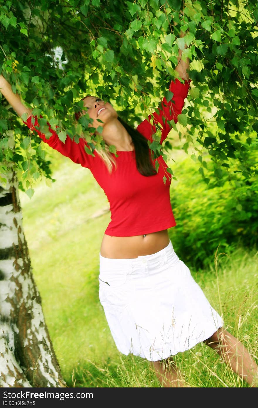 A young beautiful happy woman is laughing against a green tree and a meadow. A young beautiful happy woman is laughing against a green tree and a meadow