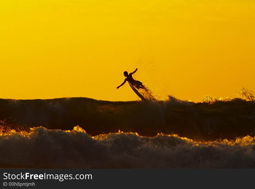 Silhouette of the surfer flying above the wave during sunset. Silhouette of the surfer flying above the wave during sunset