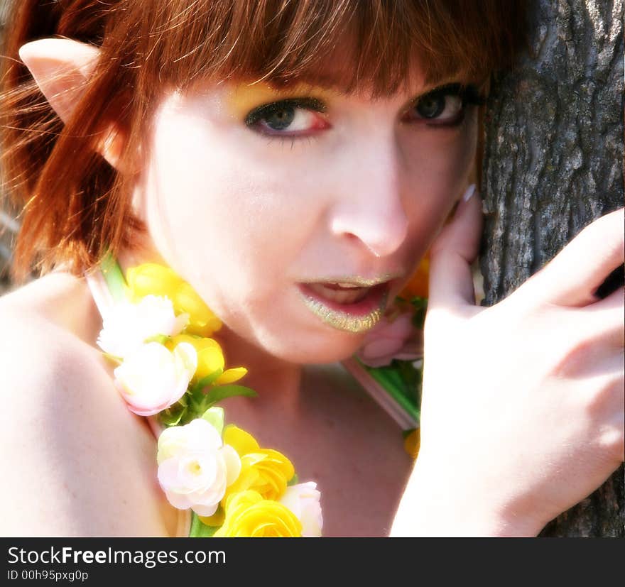 Beautiful pixie woman leaning against tree outdoors.