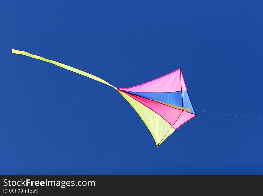 A kite flying against a blue sky in sunlight, bright colors and streaming tail. A kite flying against a blue sky in sunlight, bright colors and streaming tail