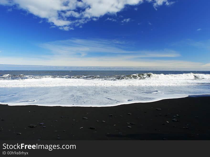 Waves crashing on a sandy black beach , deep blue sky and clouds in background. Waves crashing on a sandy black beach , deep blue sky and clouds in background