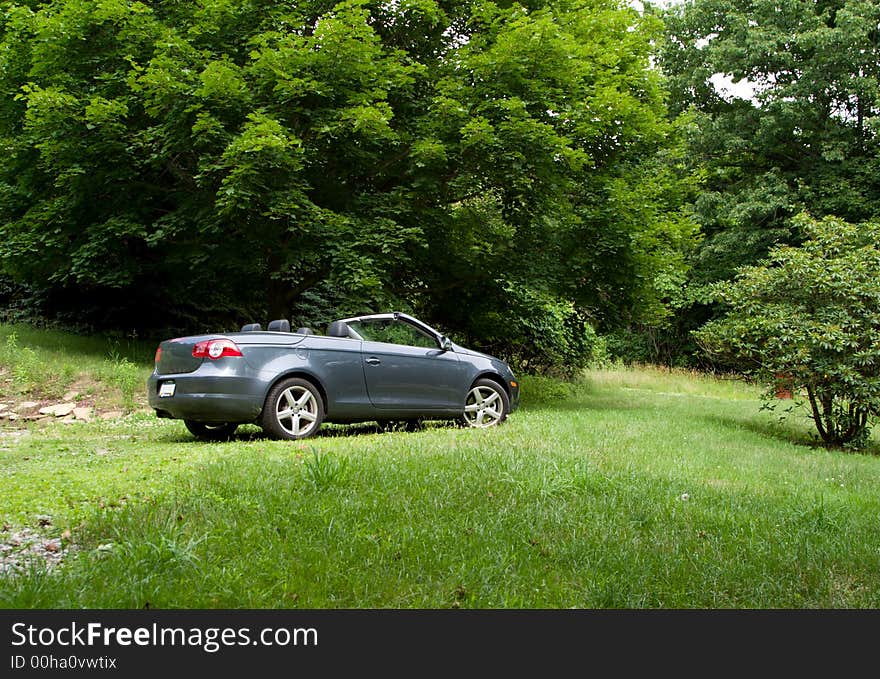 A convertible car parked in a field of grass and trees. A convertible car parked in a field of grass and trees.