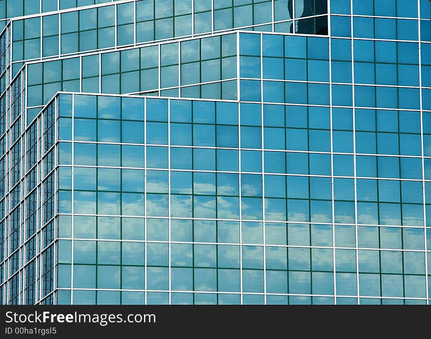 Reflection of a blue sky and clouds in the mirrored glass of a tall office building. Reflection of a blue sky and clouds in the mirrored glass of a tall office building.