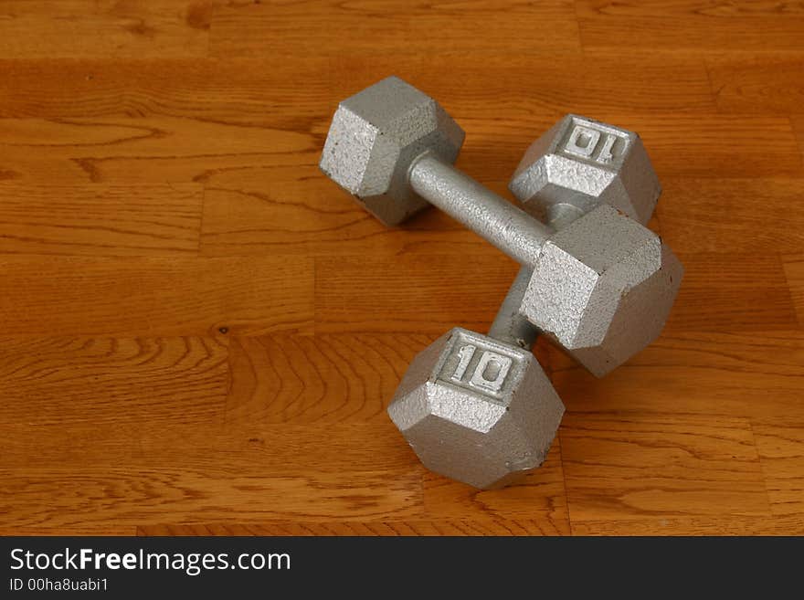 Pair of ten pound dumbells on hardwood gym floor. Pair of ten pound dumbells on hardwood gym floor.