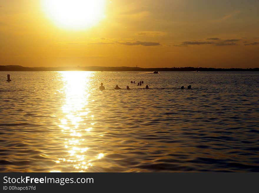 Swimmers and boaters playing on lake at sunset. Swimmers and boaters playing on lake at sunset