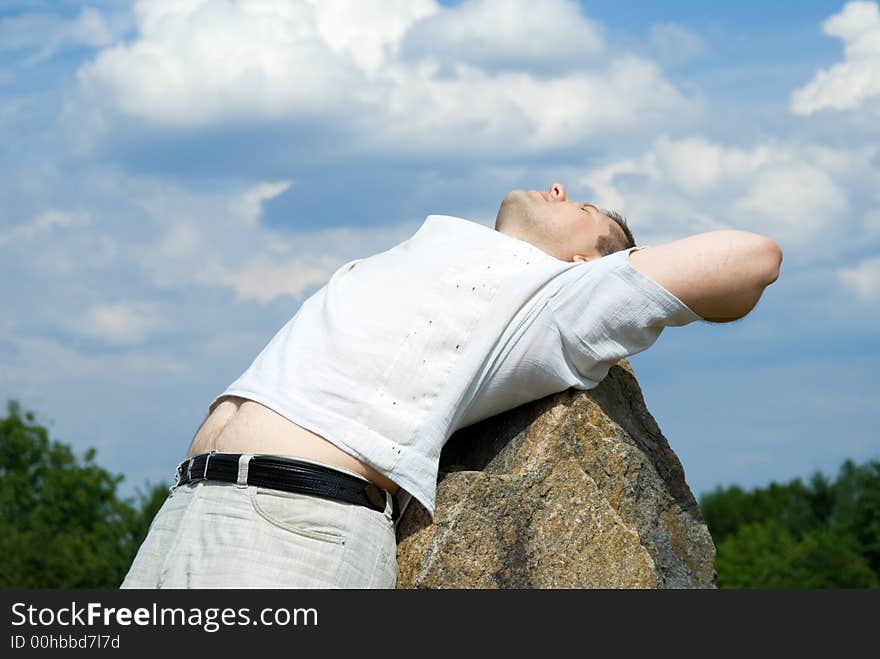 The man relaxs having put a back on a stone and looks in the sky. The man relaxs having put a back on a stone and looks in the sky