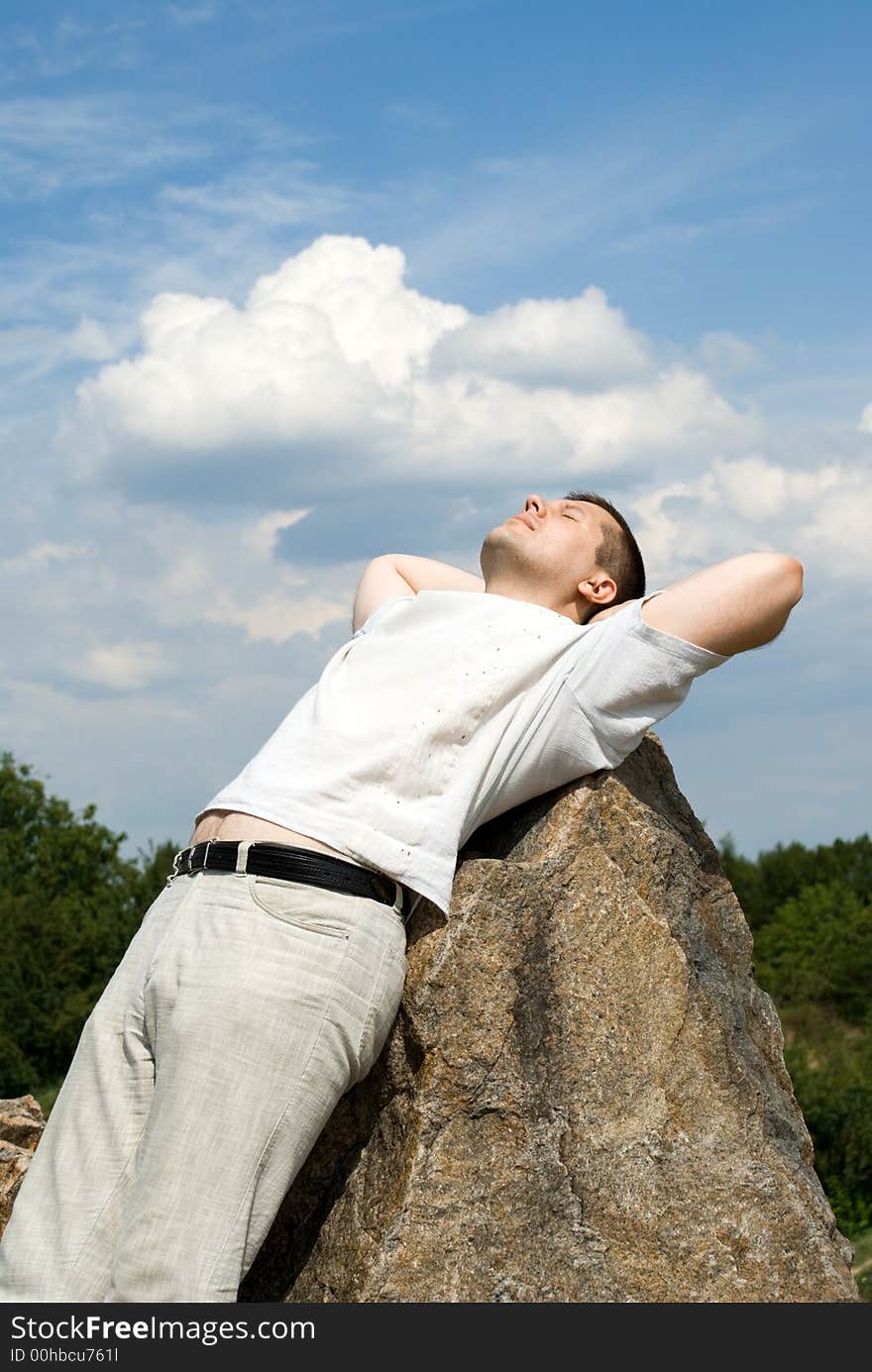 The man relaxs having put a back on a stone and looks in the sky. The man relaxs having put a back on a stone and looks in the sky