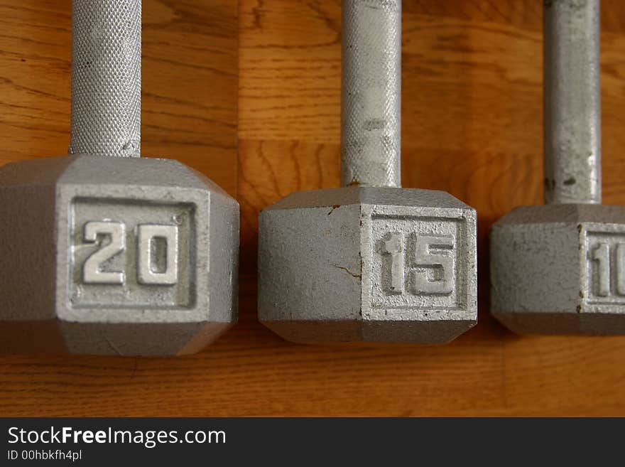 Set of three dumbells on hardwood gym floor with focus on 15 pound center dumbell. Set of three dumbells on hardwood gym floor with focus on 15 pound center dumbell.