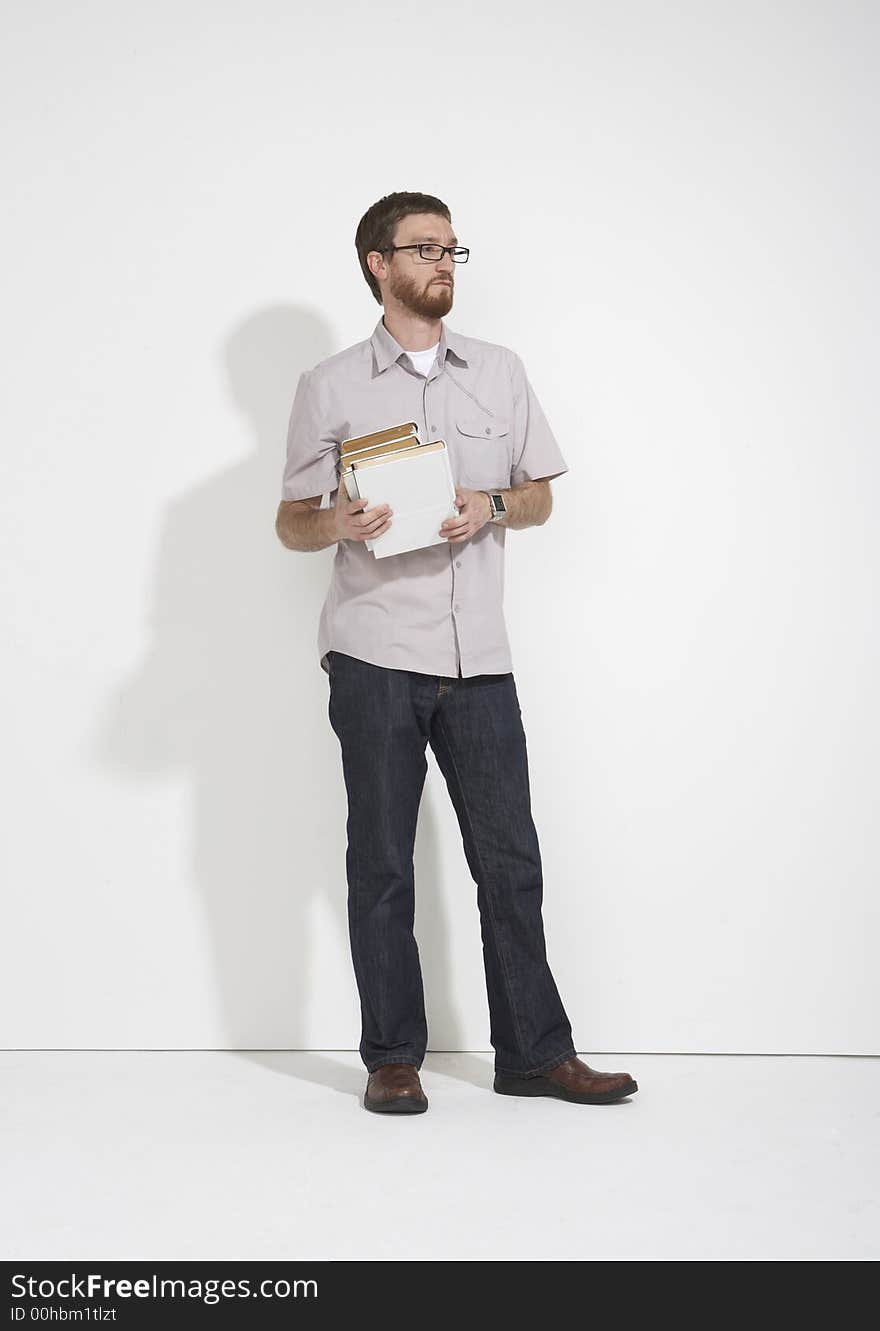 Man in a gray shirt and denim holding a stack of white books standing full length against a white studio wall. Man in a gray shirt and denim holding a stack of white books standing full length against a white studio wall.