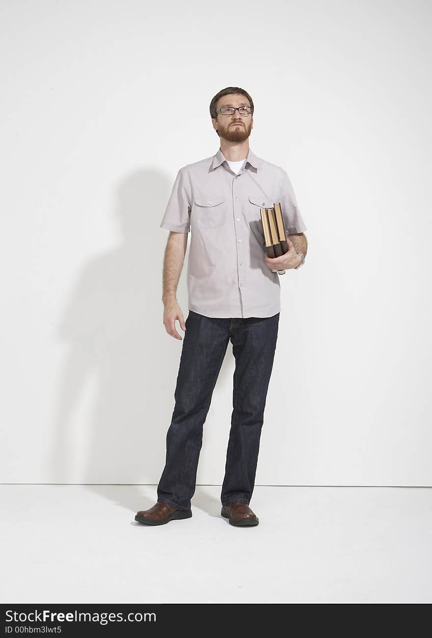 Man in a gray shirt and denim holding a stack of brown books standing full length against a white studio wall. The man is looking up in a thought. Man in a gray shirt and denim holding a stack of brown books standing full length against a white studio wall. The man is looking up in a thought.