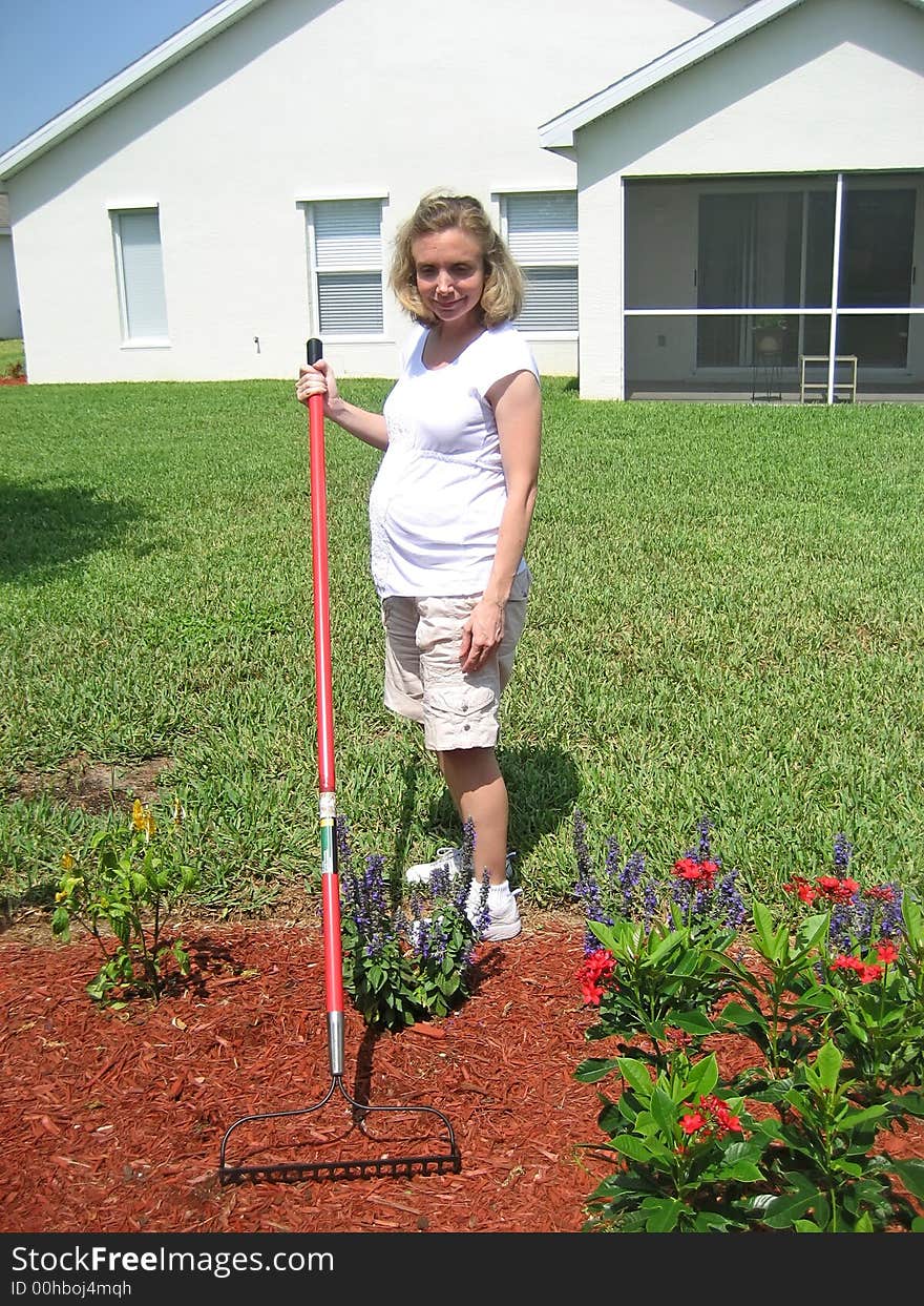 Pregnant woman with a rake in a flower garden. Pregnant woman with a rake in a flower garden.