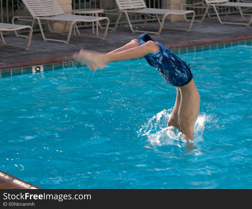Young boy diving head first into a swimming pool with head in the water and feet still in the air