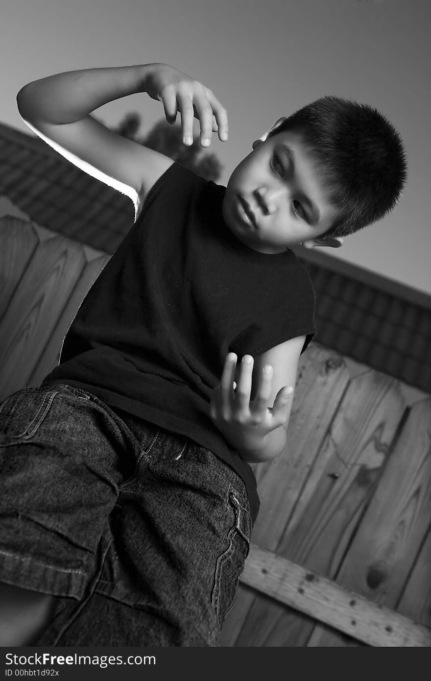 Young asian boy standing outside beside a tall wooden fence wearing jeans and black tshirt. Young asian boy standing outside beside a tall wooden fence wearing jeans and black tshirt