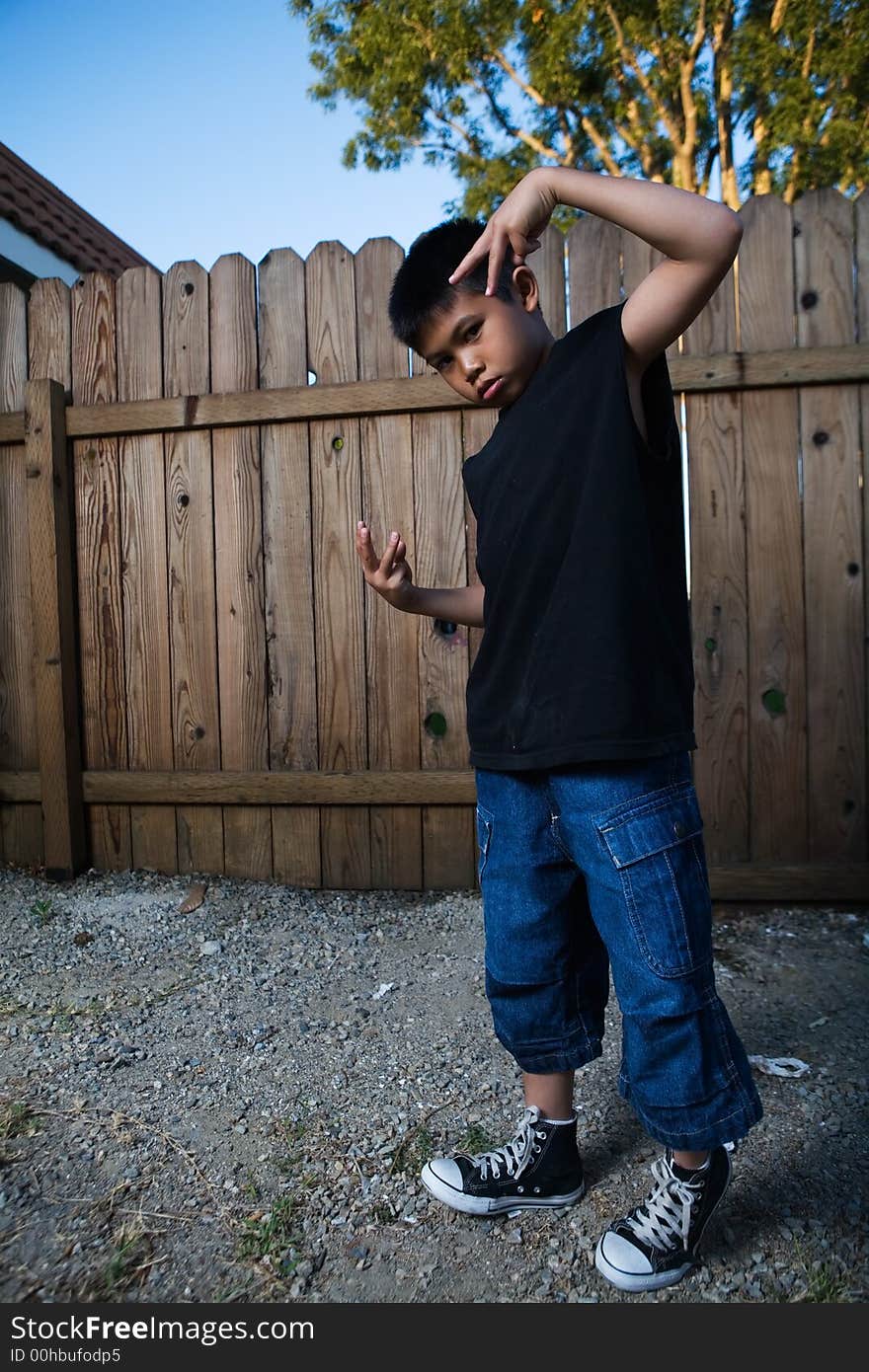 Young asian boy standing outside beside a tall wooden fence wearing jeans and black tshirt. Young asian boy standing outside beside a tall wooden fence wearing jeans and black tshirt