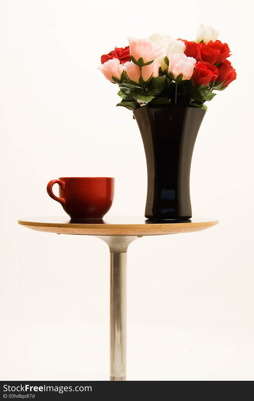 Small end table with a black vase full of red and pink roses beside a big red coffee mug. Small end table with a black vase full of red and pink roses beside a big red coffee mug