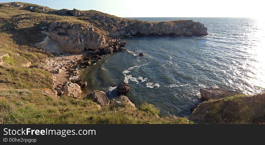 Small sea bay with sand beach and rocky borders and morning sun way highlight