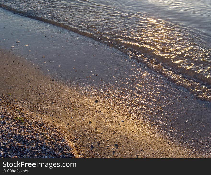 Evening sand coast surface with sunset catchlights and small wave. Evening sand coast surface with sunset catchlights and small wave