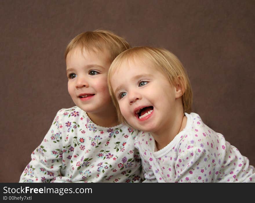 Twin sisters laugh at an onlooker during a photo session. Twin sisters laugh at an onlooker during a photo session.