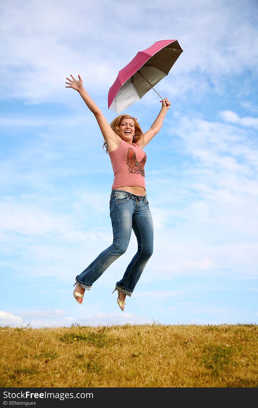 Young woman jumps with the umbrella on to the meadow