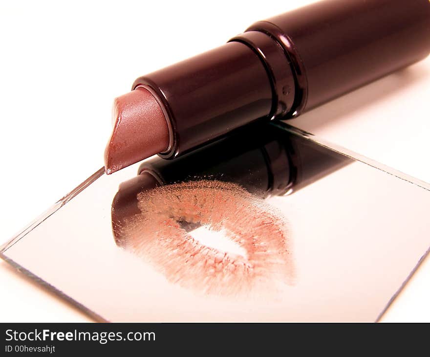 This is an image of a tube of lipstick reflected in a small, square mirror. The mirror has the impression of a woman's lips in the same color as the lipstick. This image has a white background while the mirror appears to have a slight silver tint. This is an image of a tube of lipstick reflected in a small, square mirror. The mirror has the impression of a woman's lips in the same color as the lipstick. This image has a white background while the mirror appears to have a slight silver tint.