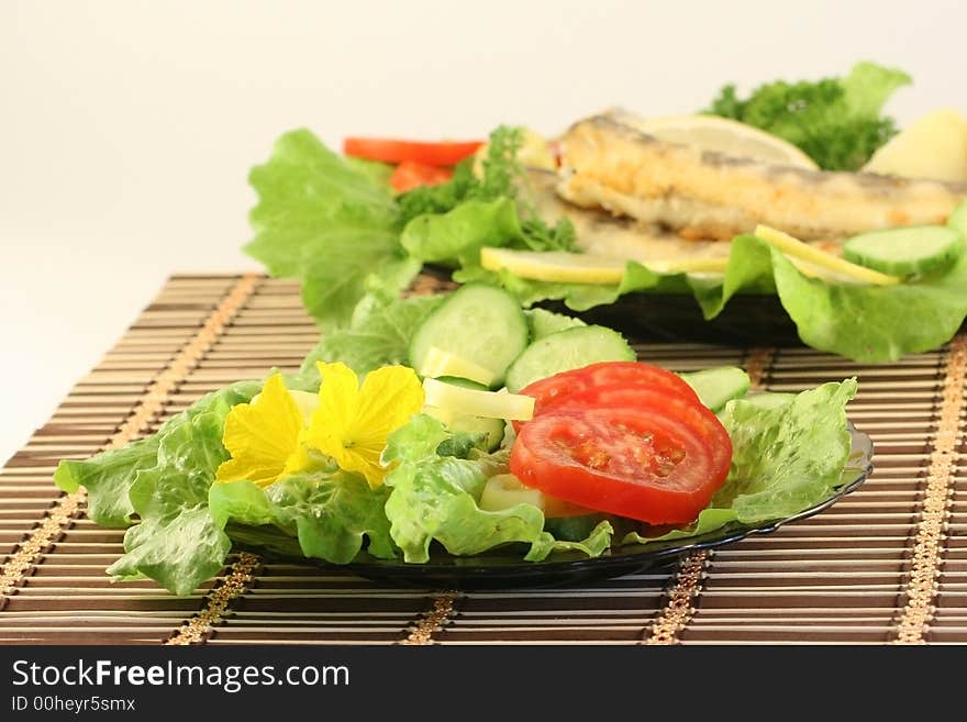 A plate with salad, on a background a dish with fried fish. A plate with salad, on a background a dish with fried fish.