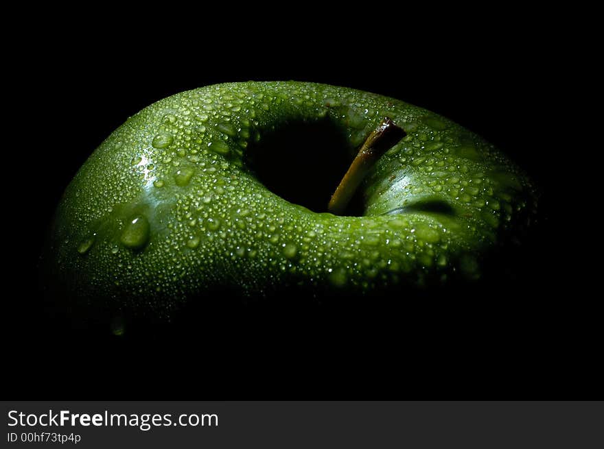 Image shows a green fresh apple in the dark, only lit by one spot light on top. Image shows a green fresh apple in the dark, only lit by one spot light on top.