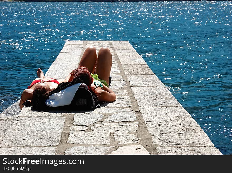 Two girls suntanning on a dock.