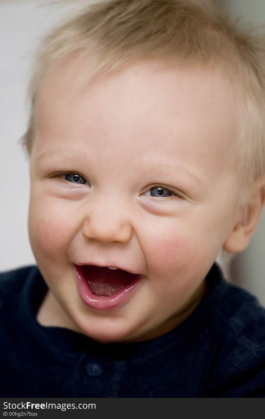 A blue-eyed baby boy in a dark blue shirt is laughing at the camera. A blue-eyed baby boy in a dark blue shirt is laughing at the camera.