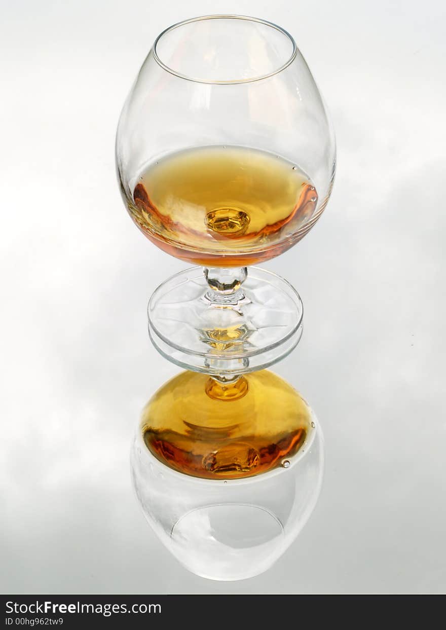 Still life with brandy glass. Reflected with cloud texture background.