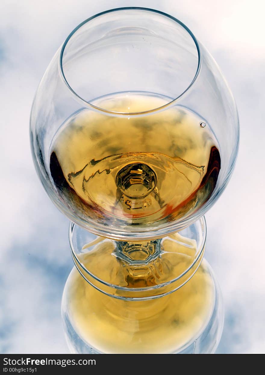 Still life with brandy glass. Reflected with cloud texture background.