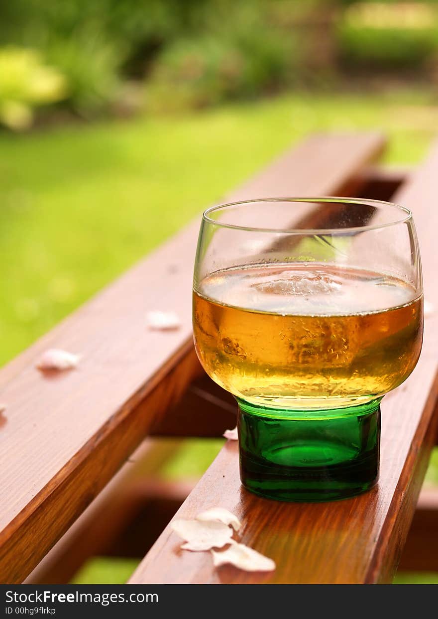 Drink in a green glass on a picnic table with garden as backdrop. Drink in a green glass on a picnic table with garden as backdrop