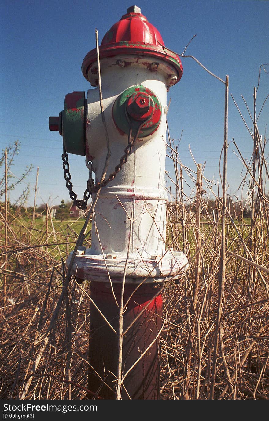 A single lone fire hydrant setting in an open field next to an area of new residential construction