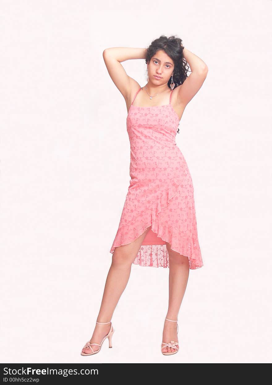 An beautiful young girl is standing in her high heels in an nice pink dress holding with both hands her long dark hair behind her head, over white. An beautiful young girl is standing in her high heels in an nice pink dress holding with both hands her long dark hair behind her head, over white.