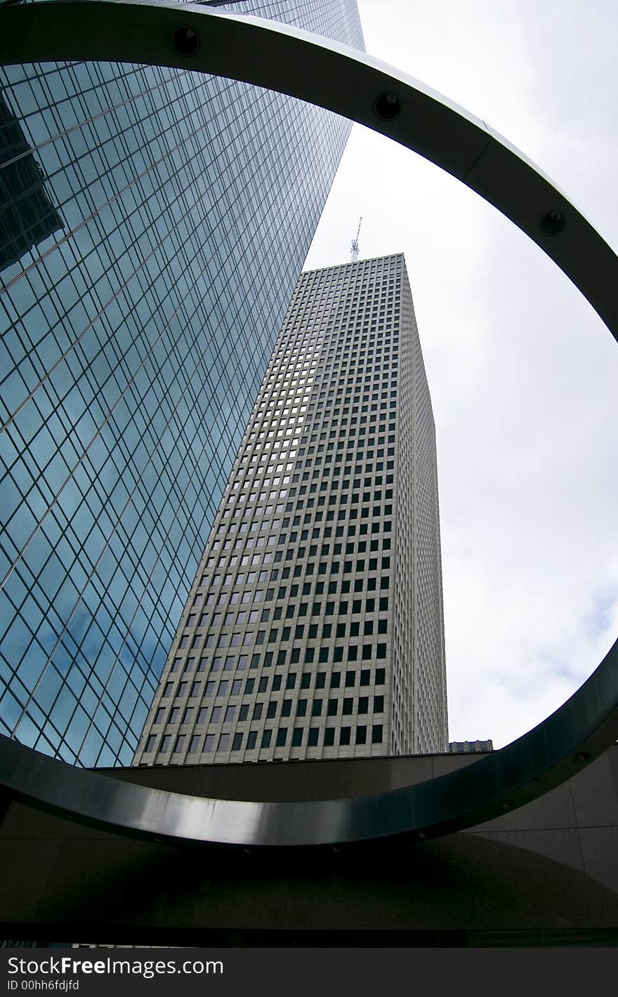 Two large skyscrapers towering above a large decorative ring on a much shorter structure. Two large skyscrapers towering above a large decorative ring on a much shorter structure.