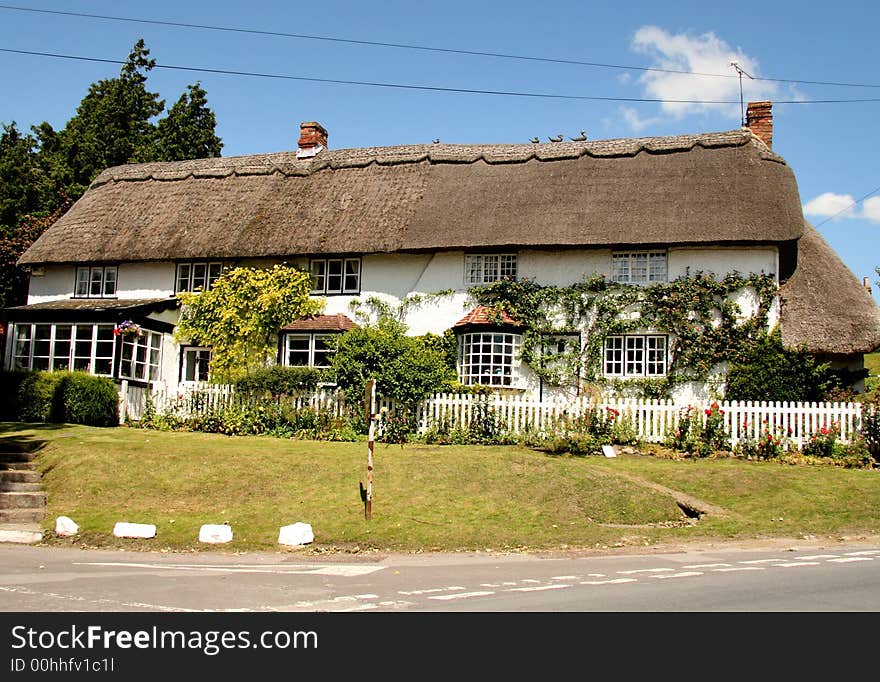 Thatched and whitewashed English Village House with picket fence in front and covered with climbing flowers. Thatched and whitewashed English Village House with picket fence in front and covered with climbing flowers